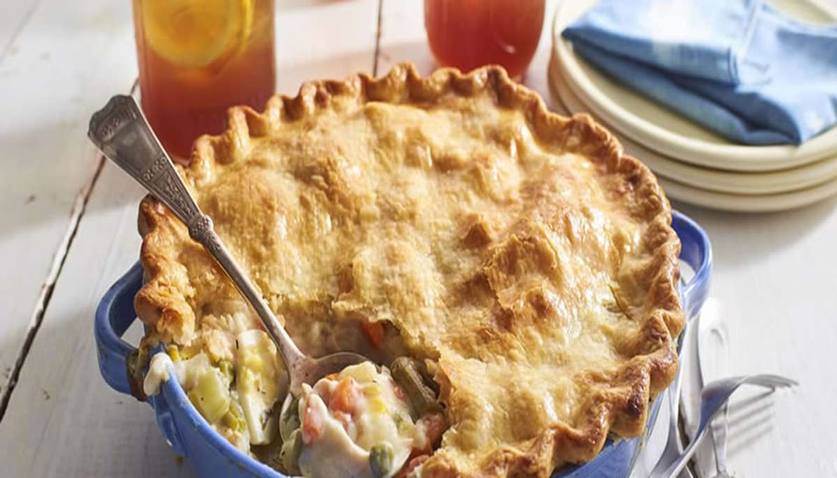 Golden-brown chicken pot pie in a blue baking dish with a flaky crust, served with iced tea — a comforting option for easy chicken dinner