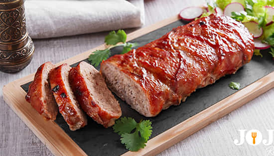 Juicy meatloaf topped with red glaze, served on a rustic table with vegetables in the background