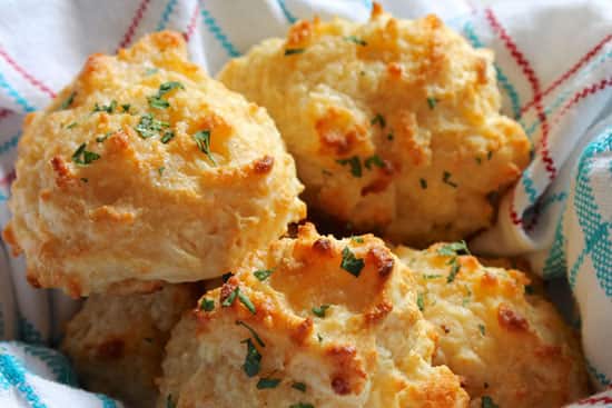 Cheesy garlic drop biscuits fresh from the oven with a buttery herb finish Fluffy cheese drop biscuits with a golden crust and herbs, wrapped in a checkered kitchen towel