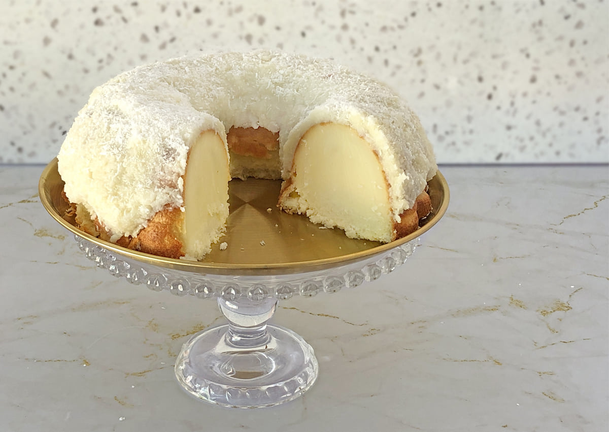 Easy coconut cake with creamy coconut topping on a glass cake stand