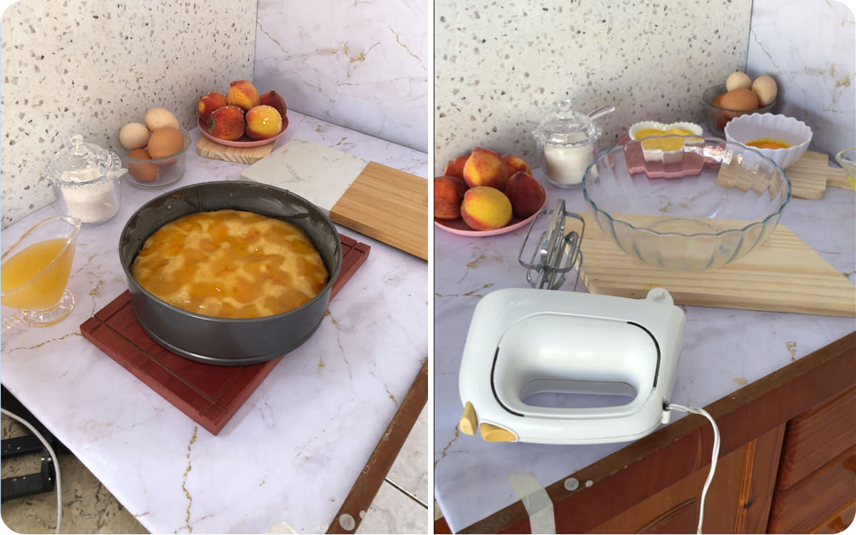 Behind-the-scenes view of the peach cake recipe, showing the batter topped with cooked peaches before baking and the kitchen setup with fresh peaches, eggs, sugar, and a hand mixer.