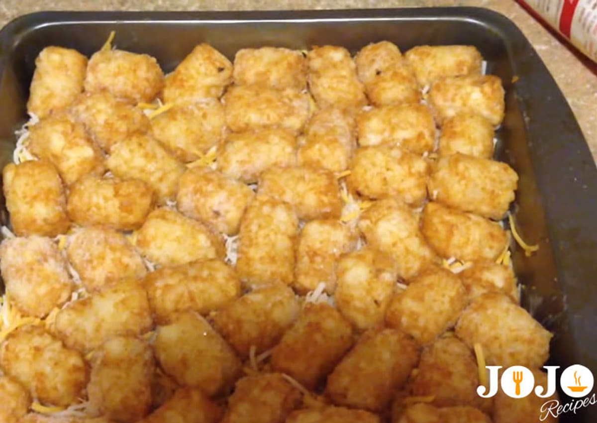 Frozen tater tots arranged over cheddar cheese in a Tater Tot Casserole with ground beef